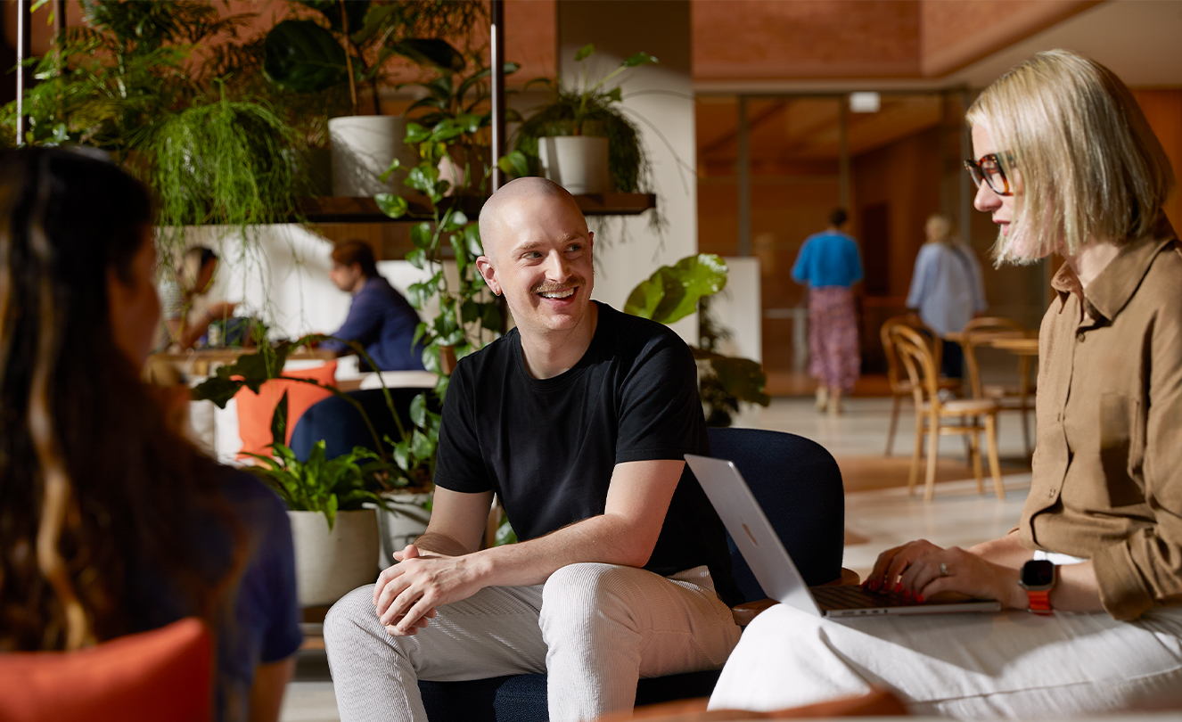 Tre Apple-teammedlemmer, en med en MacBook, taler sammen, mens de sidder i lænestole på Caffè Macs.