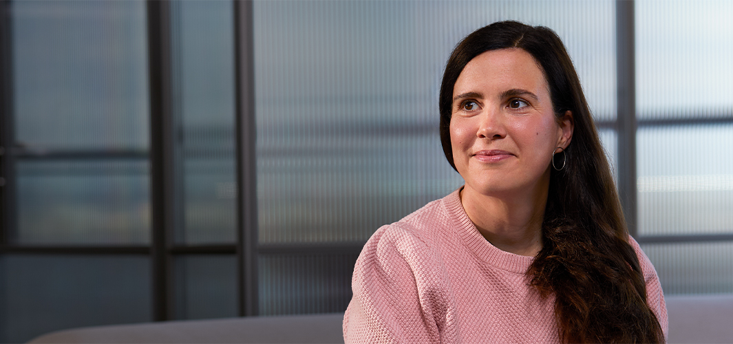 Lucie sidder indendørs med en gennemsigtig glasvæg bag sig, smiler og kigger til højre.