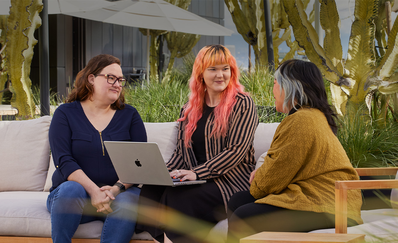 Three Apple employees, one with a MacBook, sitting together outside on a patio.