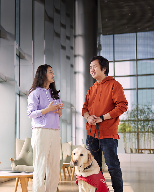 To Apple-medarbejdere taler sammen i et klart oplyst fællesrum, og den ene har en servicehund i snor.