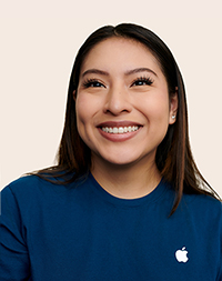 Apple Retail employee with shoulder-length hair, smiling at the camera.