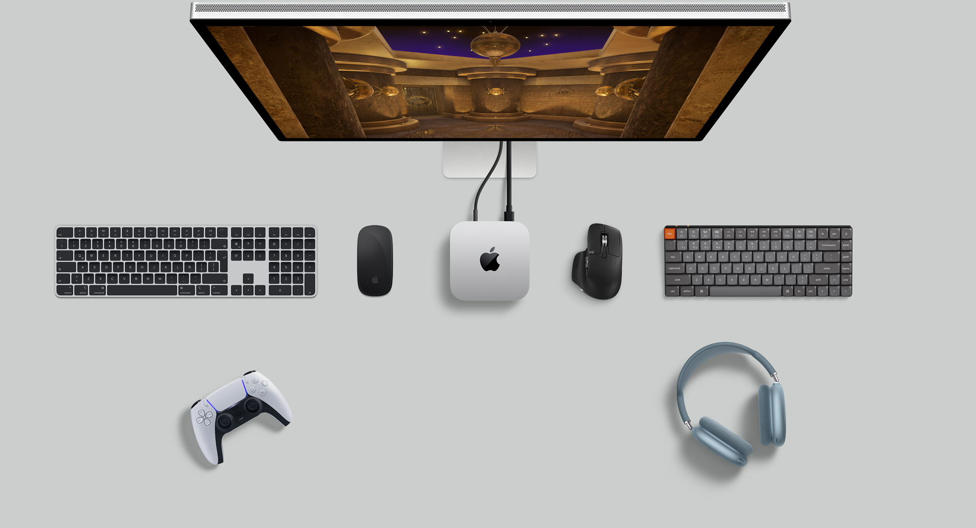 Vista desde arriba de una Mac mini color plata sobre un escritorio, con un monitor, teclados inalámbricos, dos mouse inalámbricos, un control para jugar y unos AirPods Max