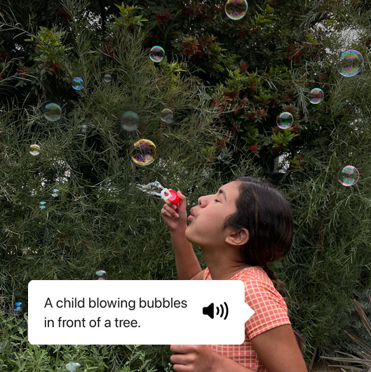 VoiceOver describing a photo and showing speech output. 'A child blowing bubbles in front of a tree.'