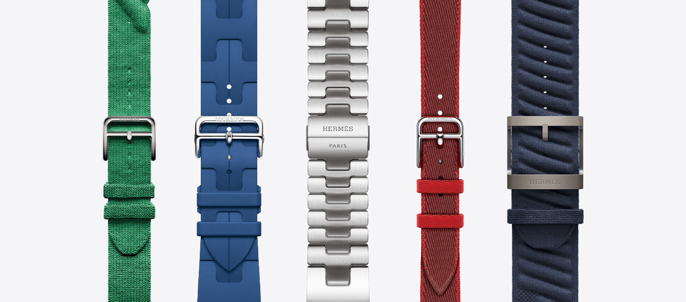 Front view of five Hermès watch straps showing a Rouge Grenat (red) Torsade, a Vert Moyen (green) Kilim, a Satiné (satin silver) Grand H, a Rouge Grenat/Vermillion (red with red trim) Twill Jump Attelage Single Tour and a Bleu Nuit (blue) En Mer.